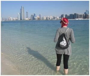 Jacqui steht im Meer vor Abu Dhabi und bewundert die Skyline.