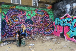 Jacqui sitzt auf einem alten Drucker vor temporären Graffitis in der Brick Lane in London, 2017.