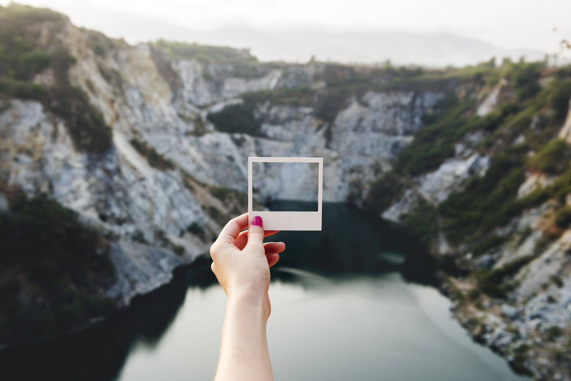 Eine Frau hält einen Polaroidrahmen vor eine Bergkulisse. Quelle: Pixabay