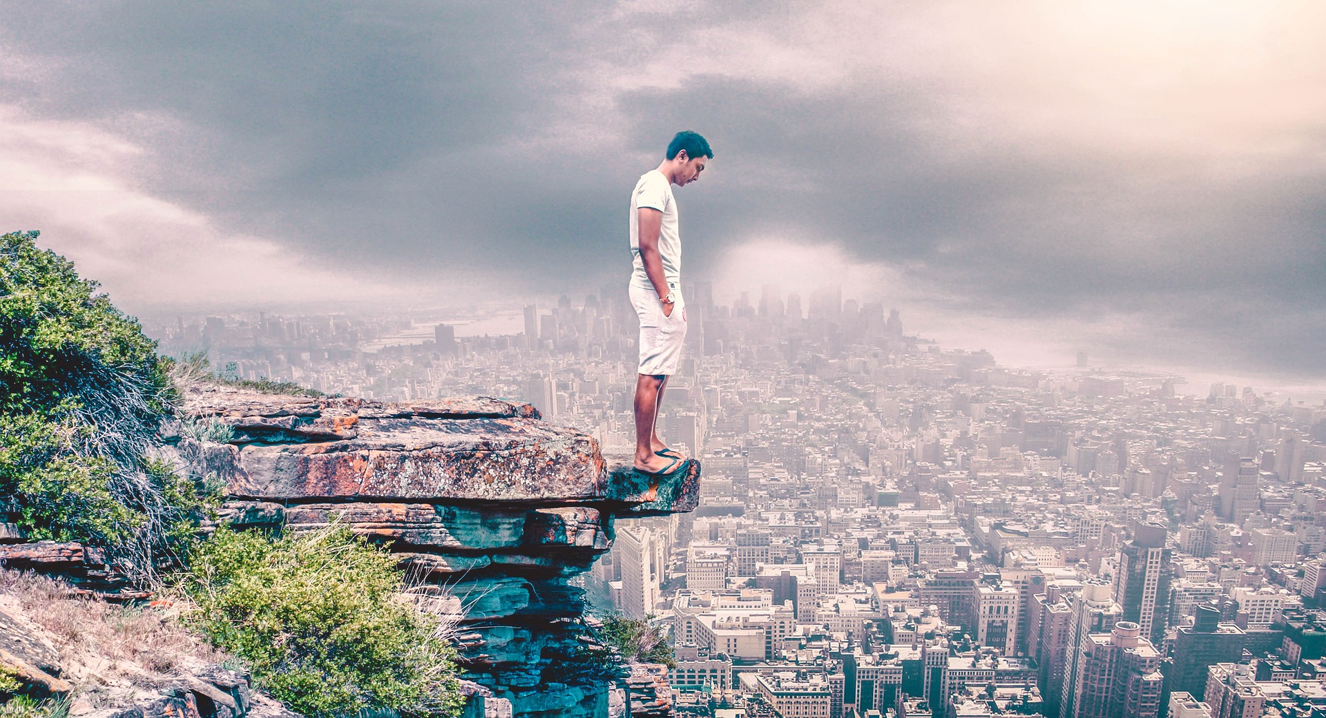 Ein Mann steht auf einem Felsvorsprung über einer Stadt. Quelle: Pixabay